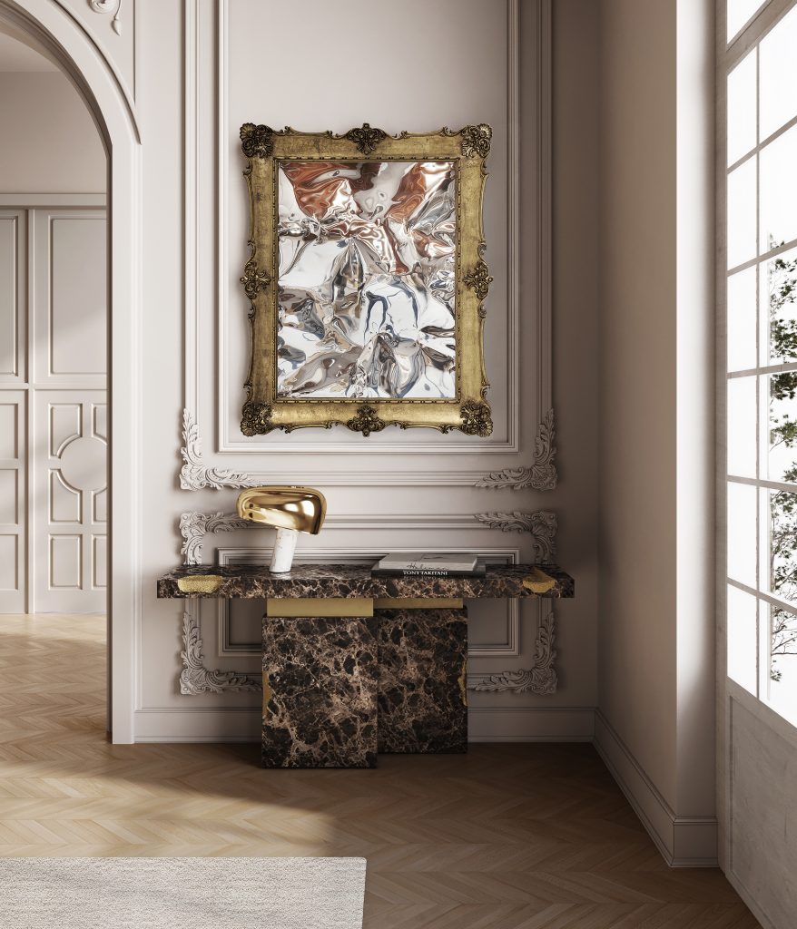 Elegant entryway with a dark marble console table, gold lamp, and an ornate framed textured mirror on classic paneled walls.
