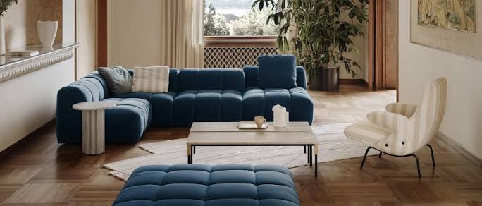 A cozy and elegant living space featuring a deep blue tufted sectional sofa, a matching ottoman, a light-colored wooden coffee table, a striped armchair, and parquet flooring luxury furniture showrooms in Singapore.