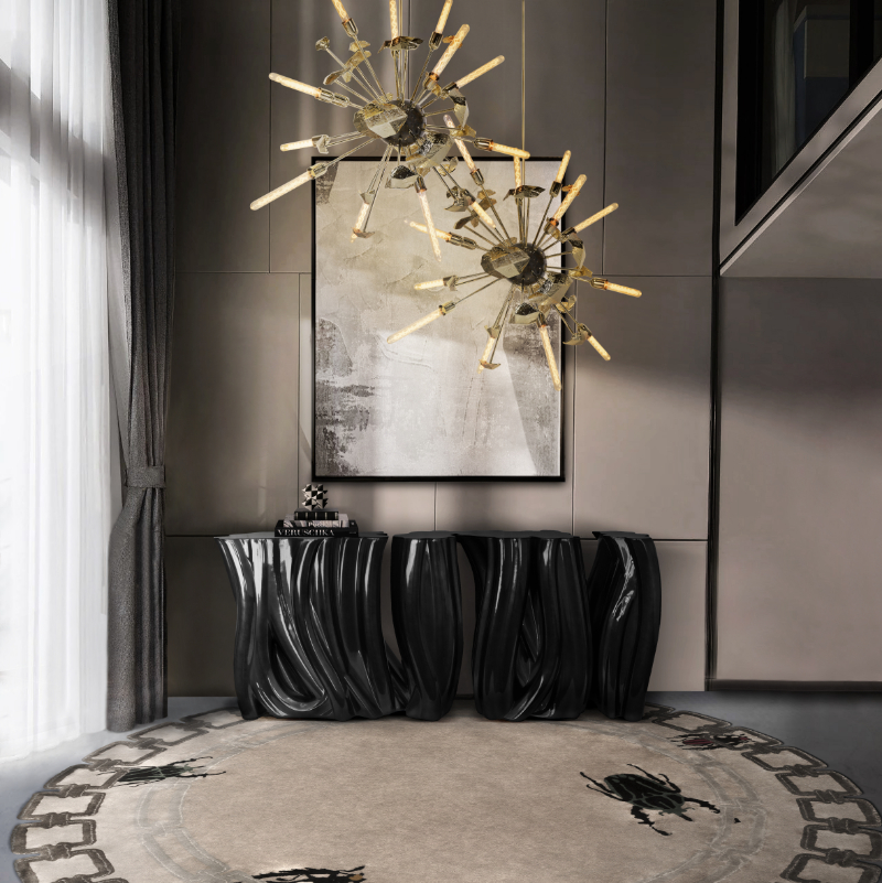 Most-Loved Pieces For Entryways - Black and grey tones for this entryway wit a round rug in grey and white, two chadeliers in gold finish, a painting on the wall and a black console.