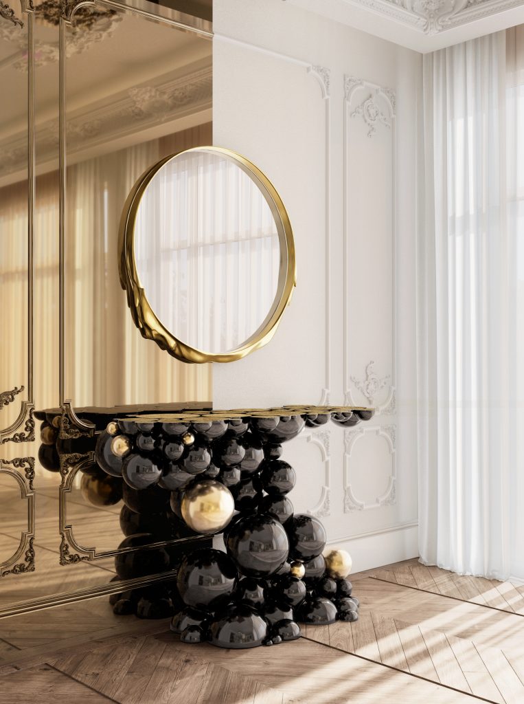 Modern Console Tables, A modern console table made of clustered glossy black and gold spheres, positioned beneath a round gold-framed mirror in a bright room with classic wall moldings.