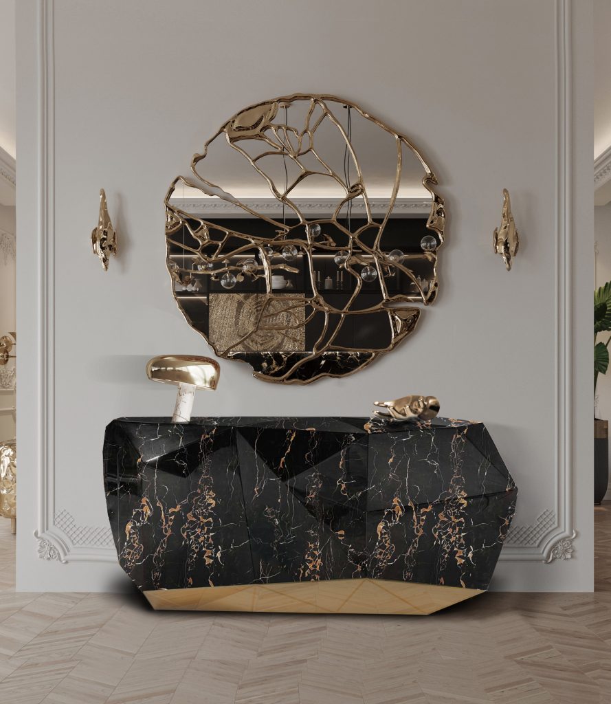 Gold and Black: Elegant Entryway with Black and Gold Decor: A luxurious entryway featuring a sleek black console table with gold accents, adorned with a stylish gold vase and black decorative items. Above the table, a large, gold-framed mirror reflects the light from an exquisite gold chandelier hanging from the ceiling. The walls are decorated with sophisticated black and gold patterned wallpaper, enhancing the overall elegance of the space. A plush black rug with gold detailing lies on the floor, welcoming guests into the opulent interior.