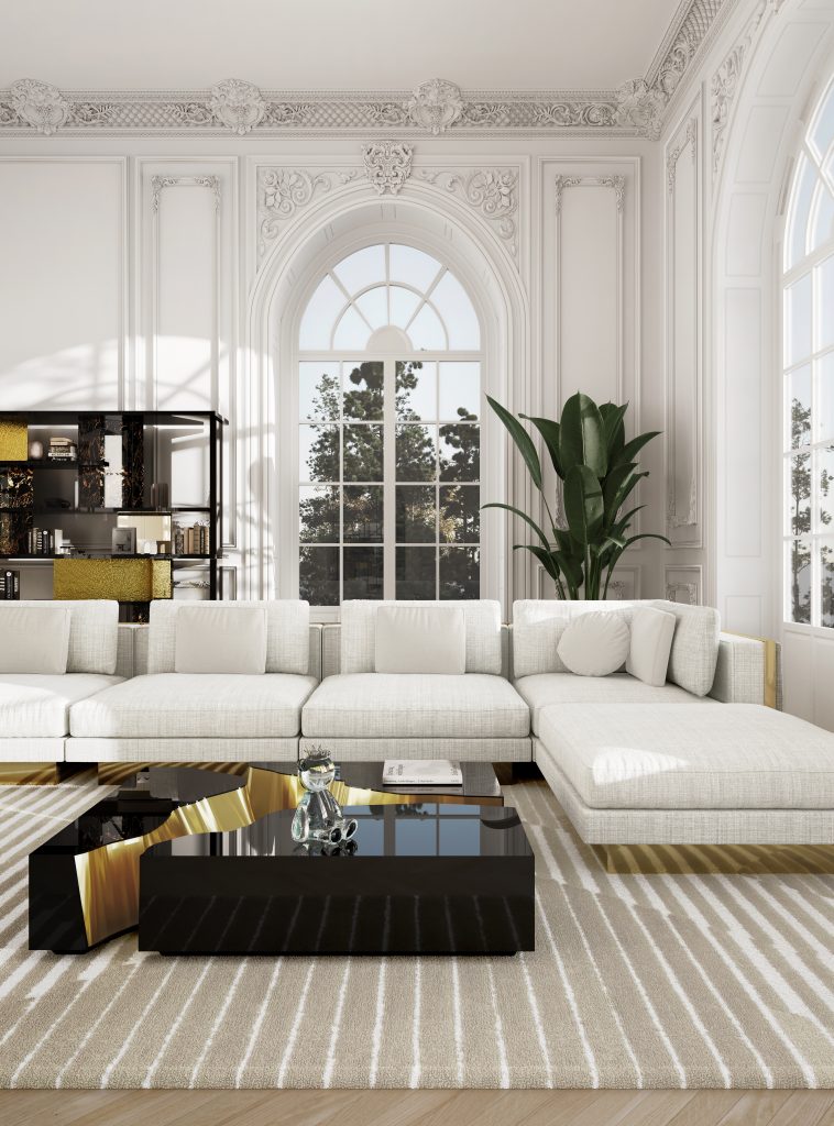luxury center tables- Elegant and bright living room with a large white sectional sofa, minimalistic cushions, and a black coffee table featuring gold interior accents. The space includes a beige and white striped rug, tall arched windows with intricate classical molding, and a high ceiling with ornate crown detailing. A tall green plant adds a natural touch, and a black and gold shelving unit decorates the background, blending modern and classic styles.