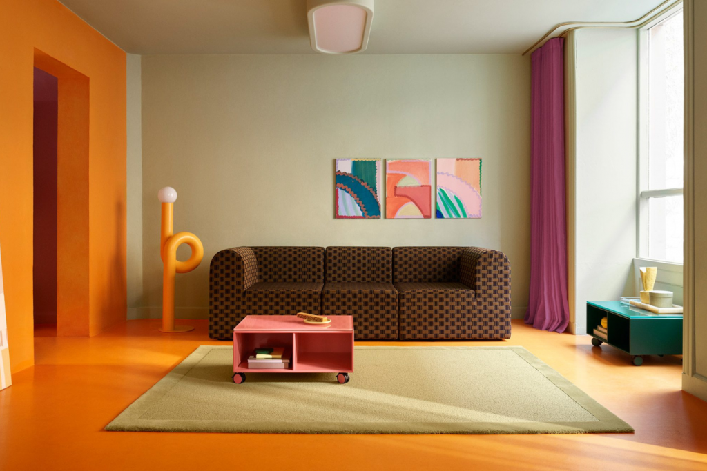 architecture events 2026, Eclectic living room interior with bright orange floors, a brown checkered modular sofa, pink coffee table, and vibrant abstract wall art.