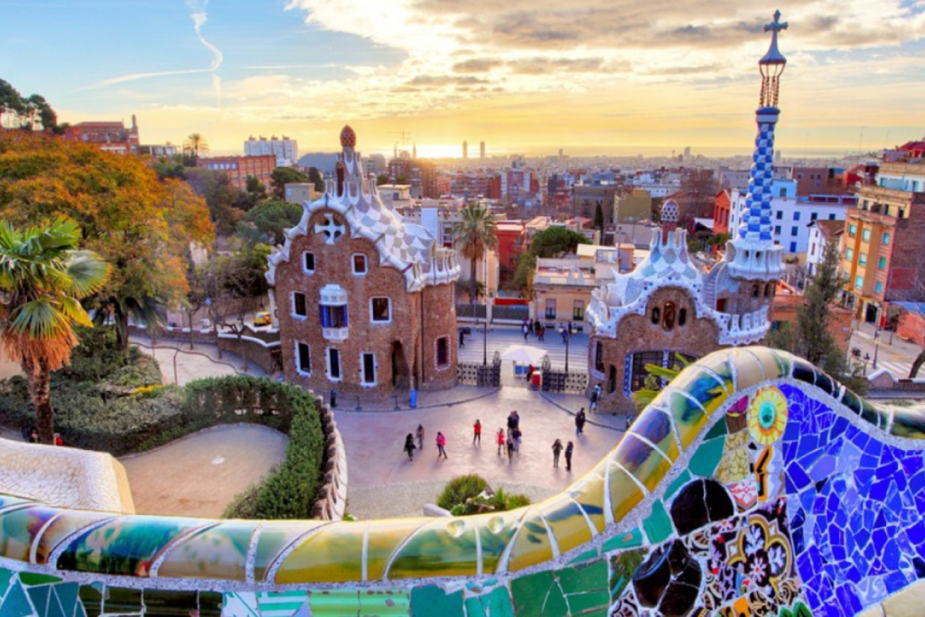 architecture events 2026, View of the gingerbread-style gatehouses at Park Güell in Barcelona, Spain, framed by colorful mosaic-tiled walls at sunset.