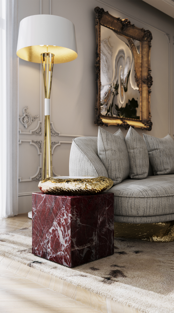 Close-up of a red marble side table with a gold textured top next to a grey tufted sofa, Levanto Rosso Marble