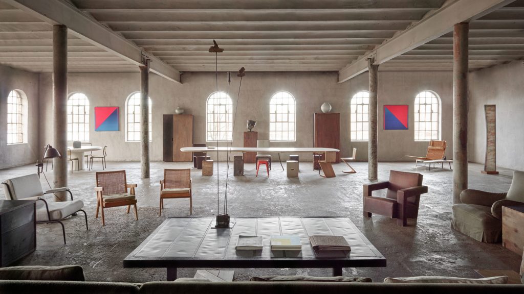 a vast, industrial loft living space with original concrete floors and columns, curated with eclectic mid-century modern and Scandinavian furniture and large, colorful geometric paintings. ELLE Decor A-List