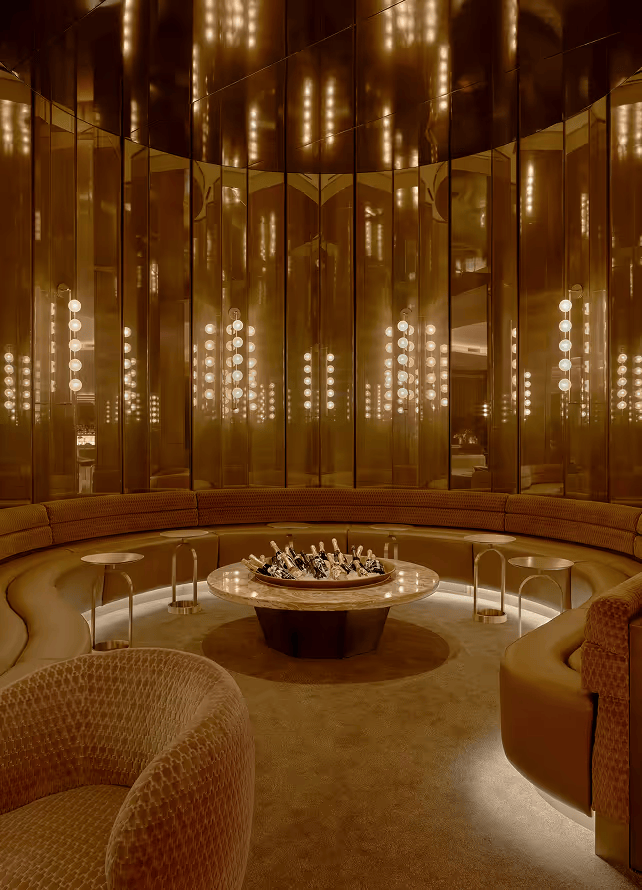 A circular lounge area with curved seating, mirrored walls, and a central table with wine buckets. ELLE Decor A-List