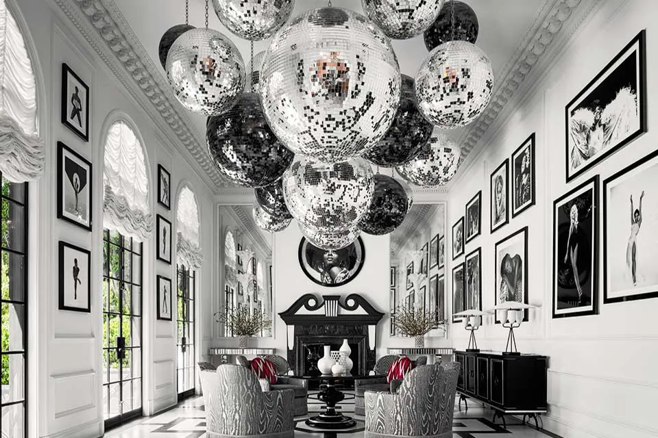 A grand, symmetrical black and white room featuring numerous disco balls hanging from the ceiling, a fireplace, and framed photographs on the walls. ELLE Decor A-List