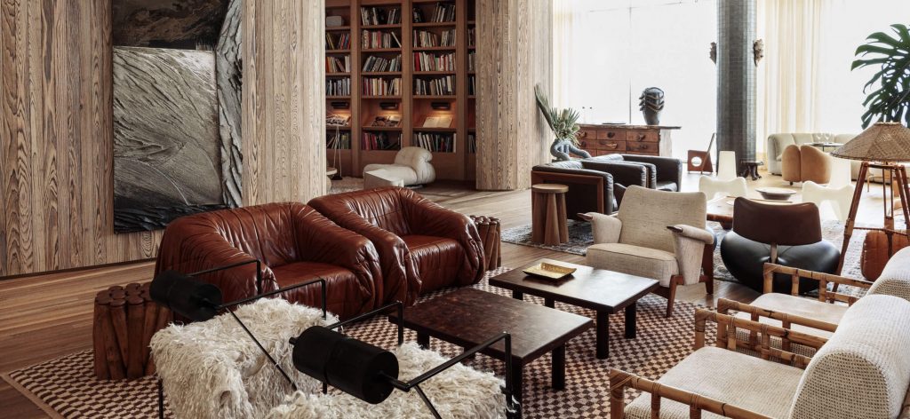 a detailed, architectural modern living space combining floor-to-ceiling vertical wood slatting, custom built-in bookshelves, chunky leather club chairs, and natural fiber accents. ELLE Decor A-List