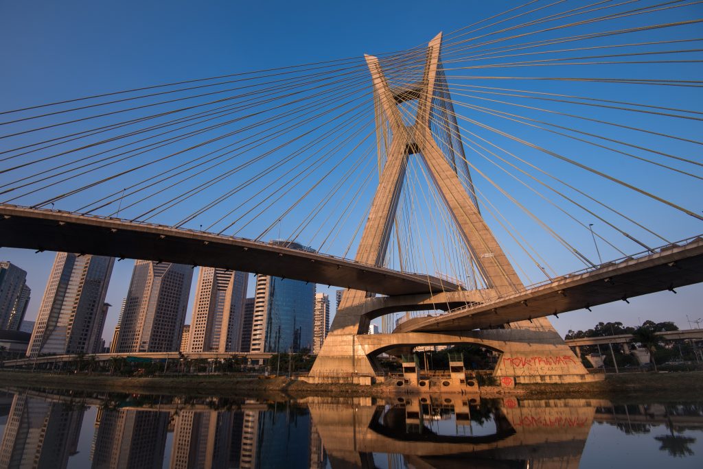Octávio Frias de Oliveira cable-stayed bridge in São Paulo with skyscrapers in the background, reflected in the river at sunset. showroom de luxo em sao paulo