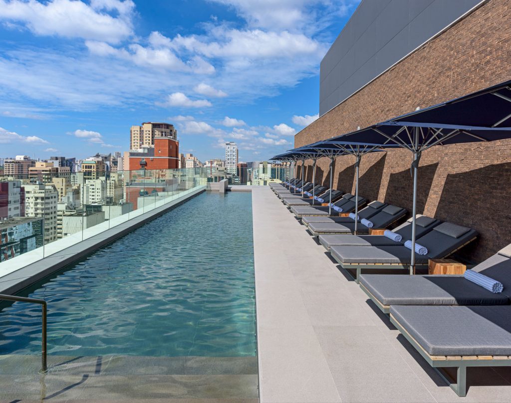 Rooftop infinity pool with lounge chairs and umbrellas overlooking São Paulo skyline – melhores hoteis em sao paulo