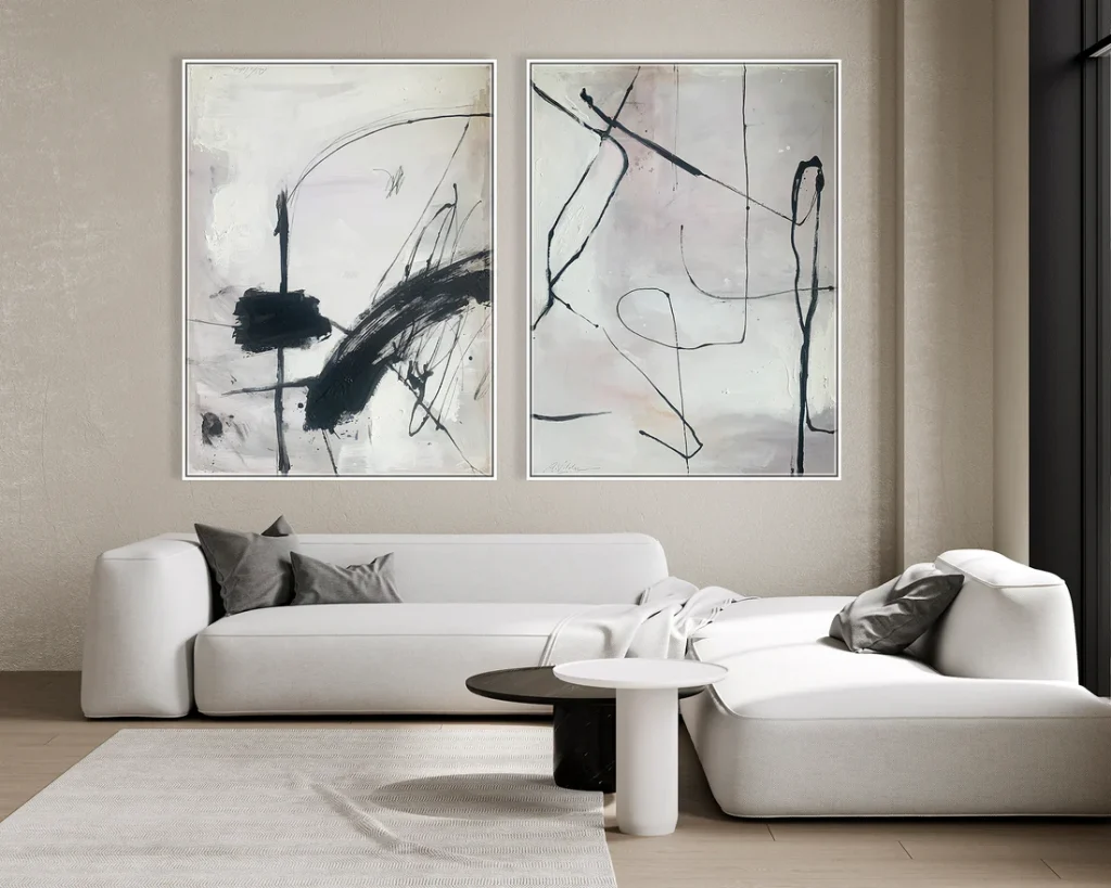 Modern minimalist living room with white L-shaped sofa, black and white abstract diptych wall art, round black and white side tables, and a beige textured rug on light wood flooring. kunal trehan