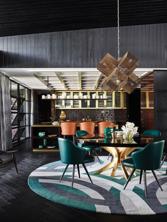 Eclectic dining room featuring teal armchairs, a round table, geometric rug, and a modern chandelier.