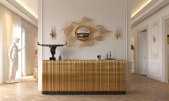 Luxurious classic interior with cream walls, ornate mouldings and herringbone wood flooring, featuring a gold fluted sideboard topped with a dark sculptural figure, candles and decor, beneath an intricate gold filigree wall mirror with matching gold sconces.