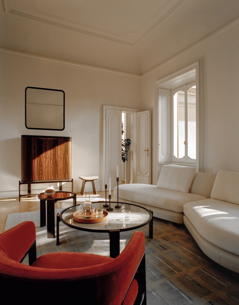 50 luxury center tables - nude curved sofa and a red-ish armchiar in the middle two round center tables with wood frame and a glass top, at the back a wodded cabinet