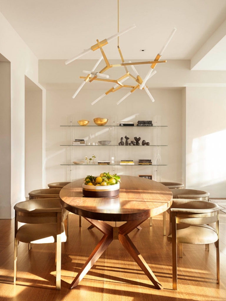 Pembrooke & Ives - A wooden dining table, dining chairs and a glass bookcase. A large suspension lamp on with gold details on the ceiling.