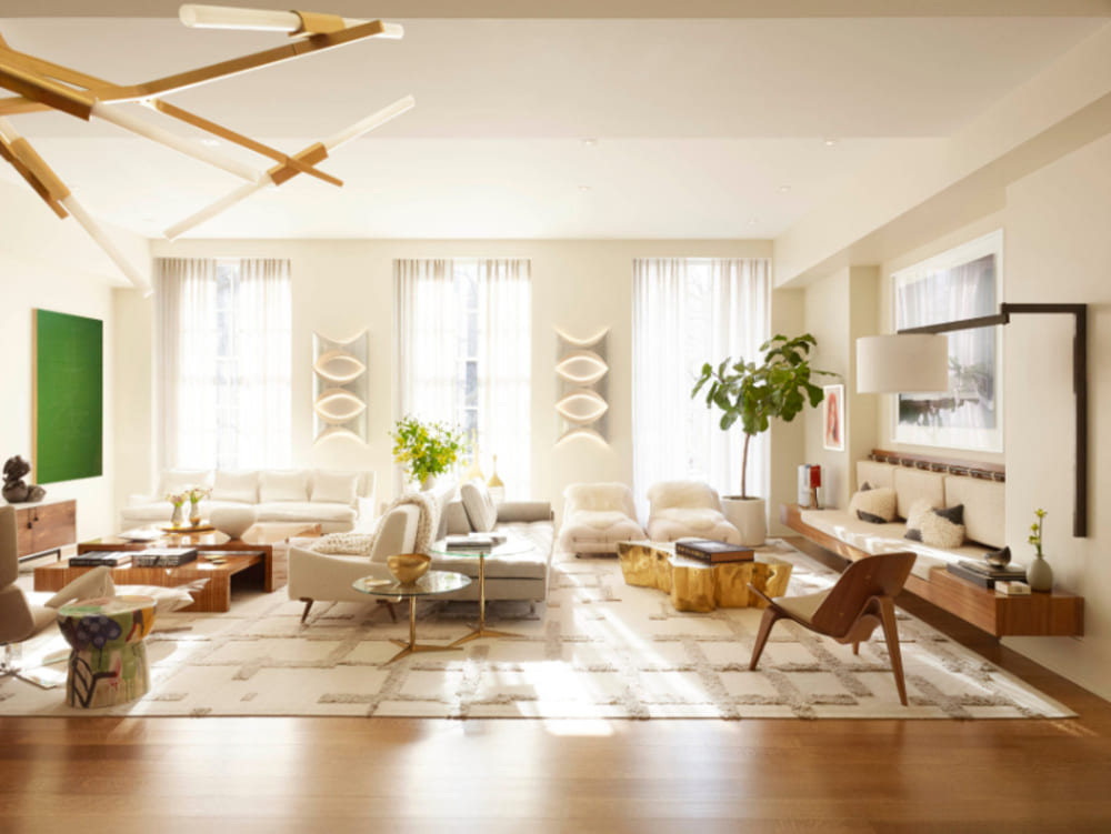 Pembrooke & Ives - A clean look living room with wooden and gold materials. A green paiting on the wall, three sofas, two enter tables and four armchairs.