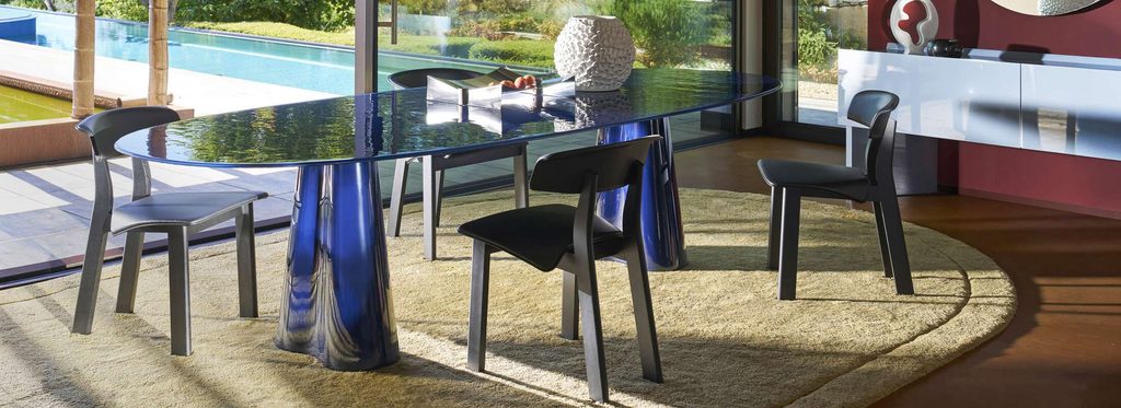 Dining room featuring an oval translucent blue glass dining table surrounded by dark chairs.