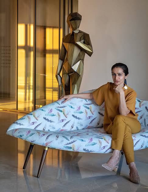Designer on patterned sofa with sculpture, luxury interior designers in India