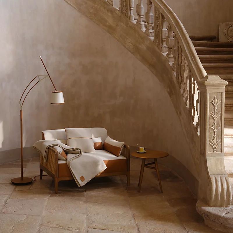 Cozy reading nook under a stone staircase with a wooden armchair, floor lamp, and side table.