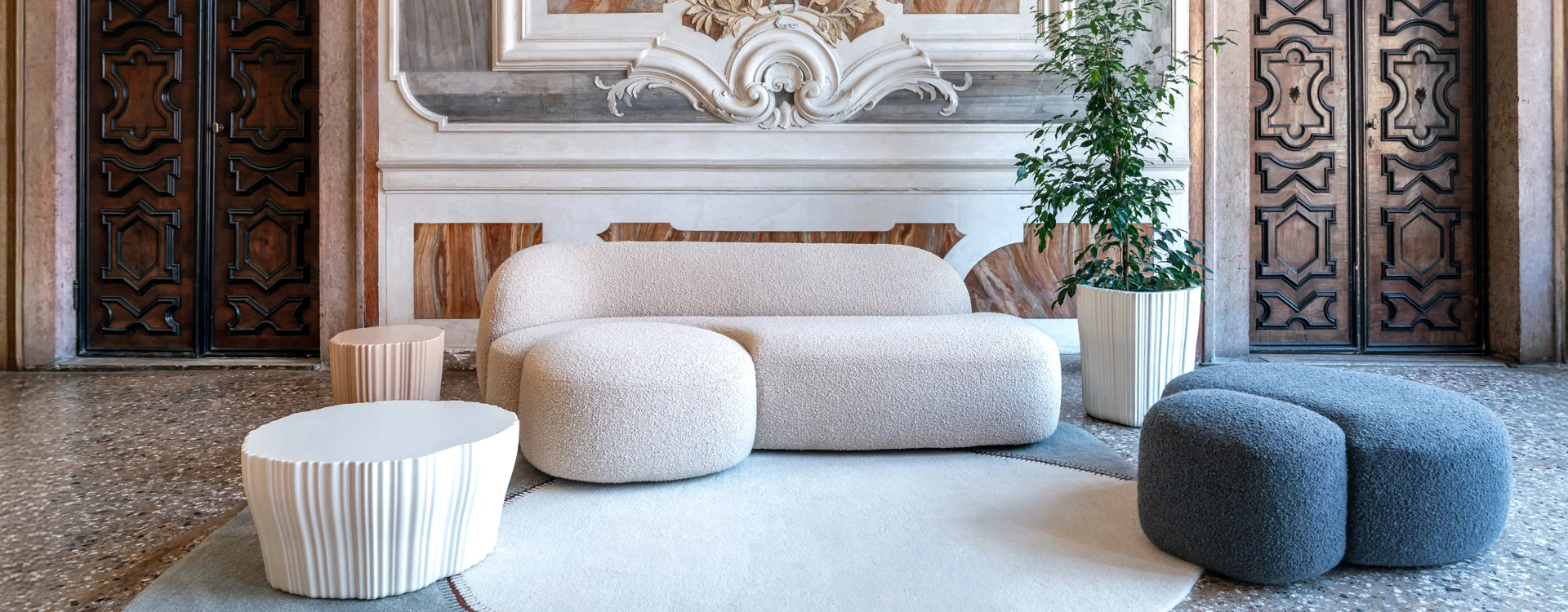 Modern curved bouclé sofa with matching ottomans and side tables in a historic interior set.