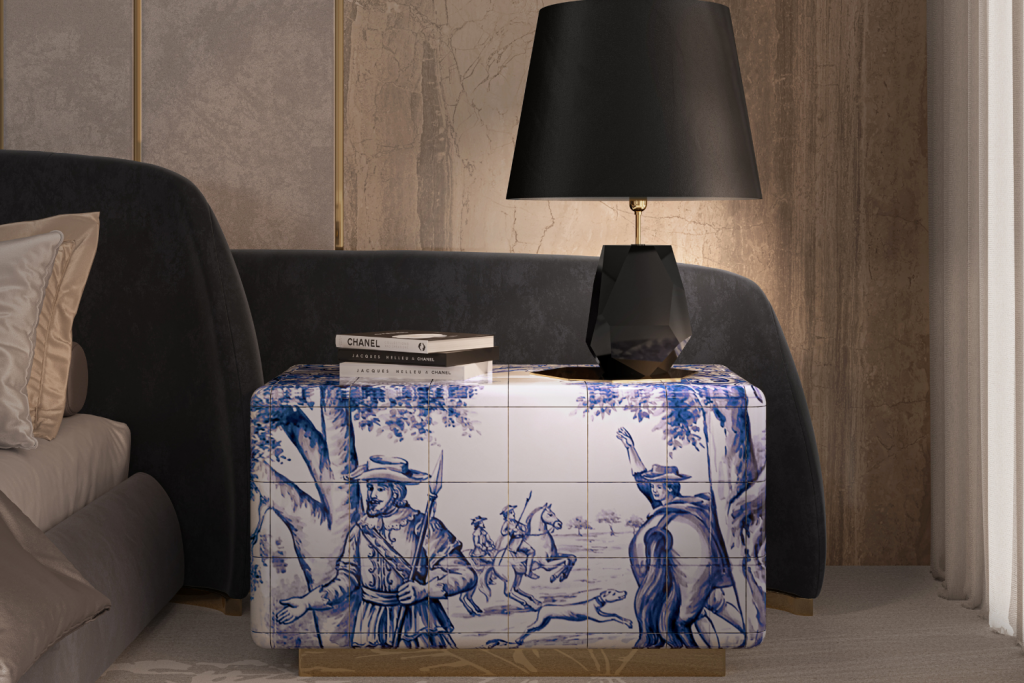 Elegant bedroom corner featuring a nightstand with blue-and-white tile artwork, topped with fashion books and a black geometric lamp beside a dark upholstered bed.