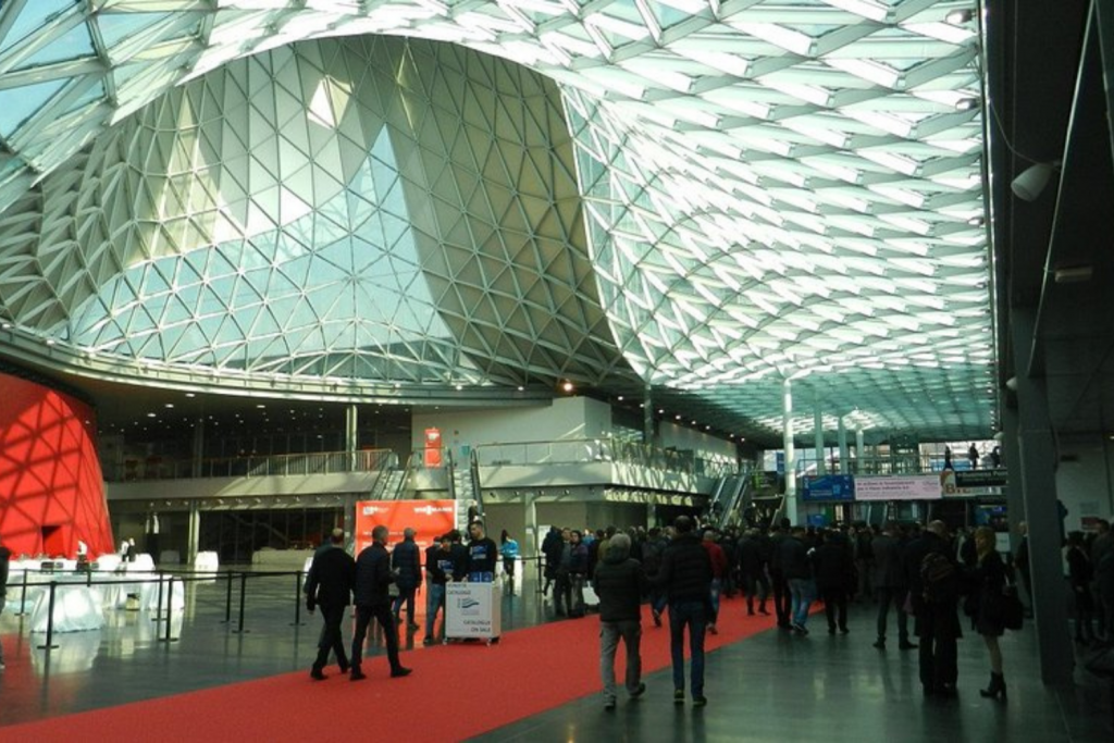 Salone del Mobile exhibition hall in Milan with contemporary architectural ceiling structure and visitors exploring the international design fair. Milan Design Week 2026