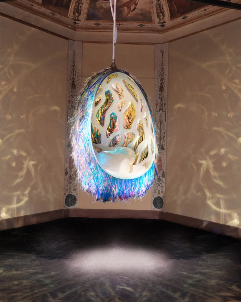 Hanging iridescent "egg" chair with a golden interior in a room with frescoed ceilings. Objets Nomades