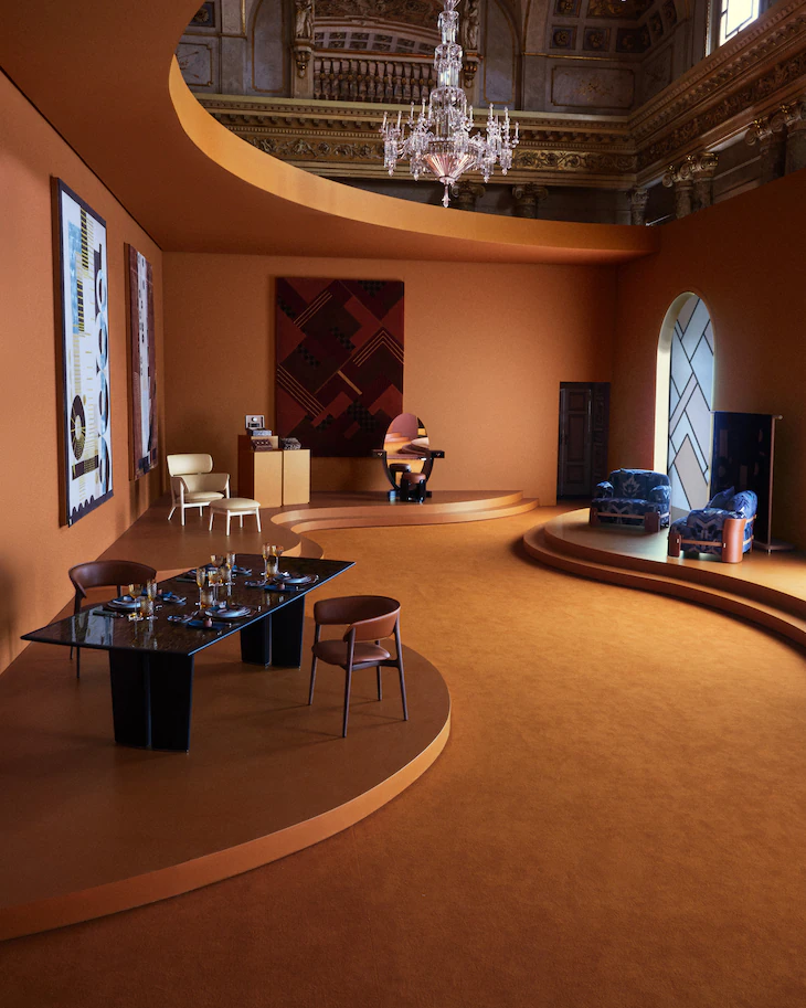 Monochromatic orange room featuring tiered platforms with designer furniture and a crystal chandelier. Objets Nomades