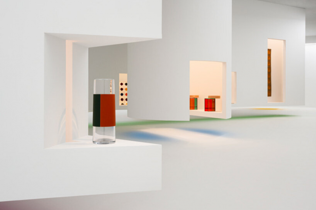 Design Week fashion events, minimalist exhibition installation featuring sculptural glass objects presented within architectural white gallery environment.