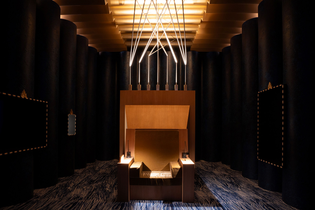 Dramatic scenographic installation with architectural lighting, dark columns and sculptural central seating composition, Salone del Mobile exhibitions