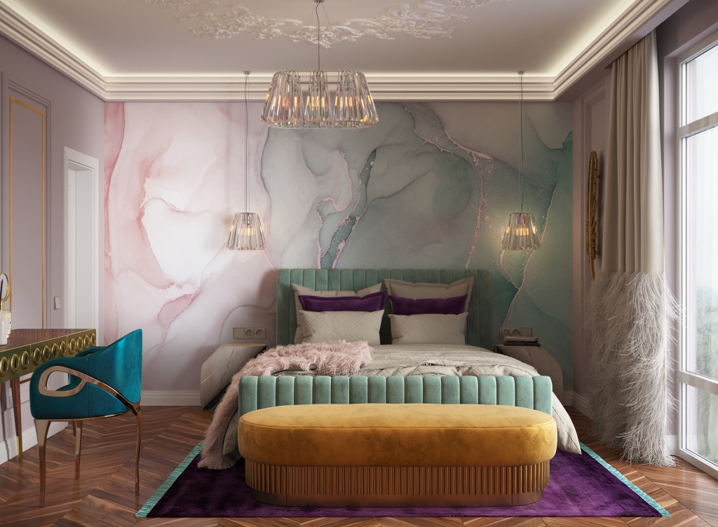 A modern bedroom featuring a prominent fluid watercolor-style wallpaper in pink and green hues behind a teal ribbed bed. A long mustard-yellow velvet bench is positioned at the foot of the bed on a purple rug. A teal velvet vanity chair stands to the left under a contemporary glass chandelier. luxury bedroom