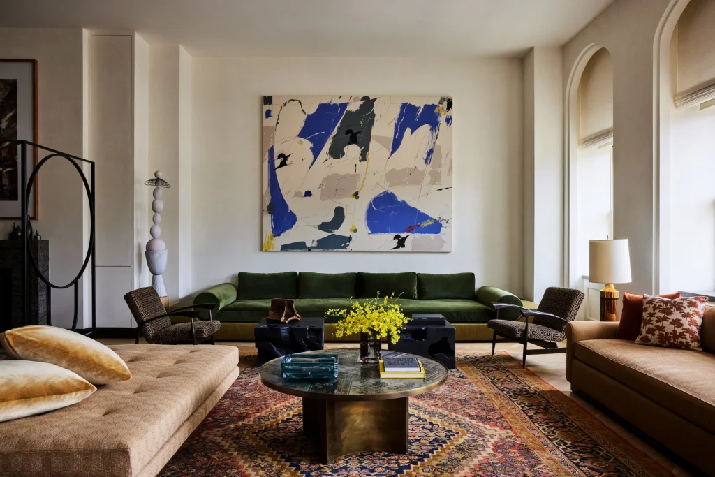 A sophisticated living area showcasing a vibrant green velvet sofa, a large abstract painting on the wall, and a patterned area rug under a round coffee table, arranged by interior designers.