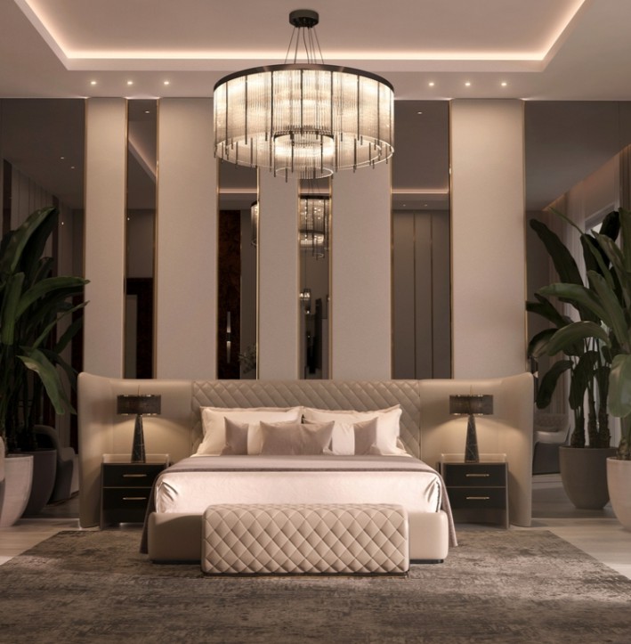 A truly opulent bedroom with a grand, oversized bed centered in the frame. The headboard is upholstered in a deep, plush velvet and features intricate gold tufting. An ornate crystal chandelier hangs from the ceiling, casting a warm glow. The walls are covered in rich, damask wallpaper. Luxury bedroom.