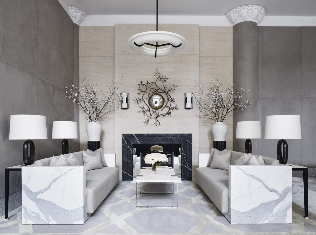 A symmetrical luxury lobby or living room with two identical marble-sided sofas facing each other, centered around a black marble fireplace and gray wall panels, designed by interior designers