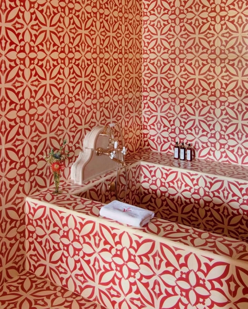 A bathroom corner featuring walls and a bathtub completely covered in a vibrant, geometric red-and-white tiled pattern, complete with classic brass fixtures. Vermelho Hotel