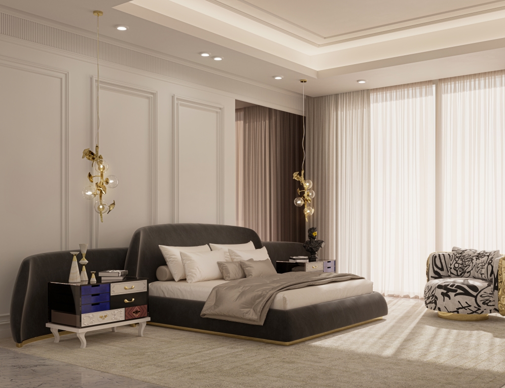 Spacious and bright luxury bedroom with neoclassical wall moldings and large sheer curtains. The low dark gray upholstered bed features an extended wrap-around headboard. To the left sits a highly artistic nightstand with asymmetrical drawers in white, blue, black, and wood finishes with classical legs. Two delicate golden branch pendant lights hang from the ceiling, and a graffiti-patterned armchair rests to the right. luxury bedrooms