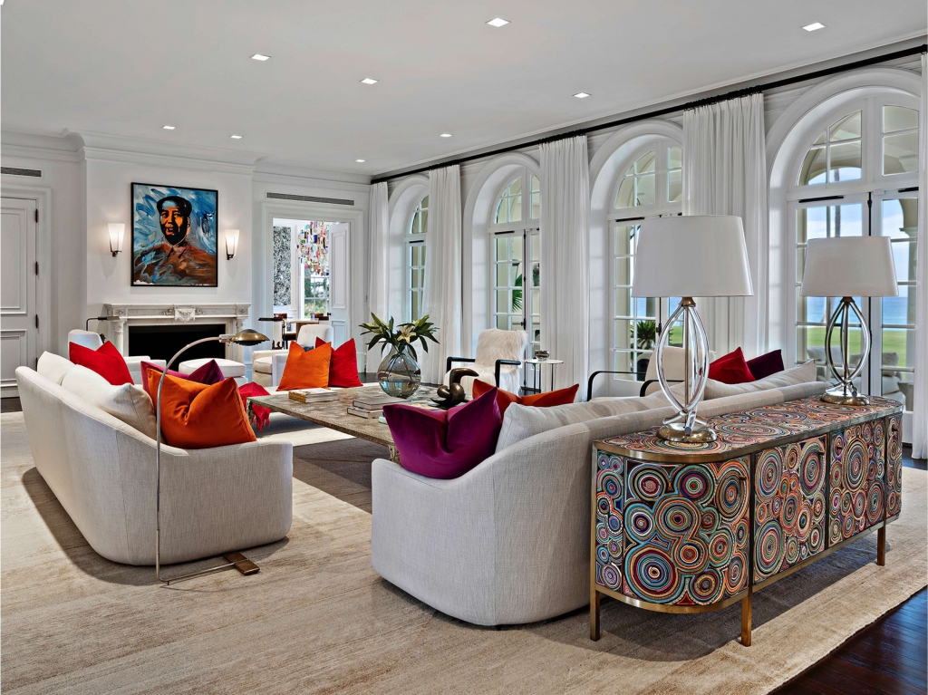Elegant high-ceiling living room with large white arched doors opening to the garden, decorated with clean-lined sofas and vibrant pillows in red, orange, and purple, complemented by a curved sideboard with a colorful geometric pattern in the foreground, interior designers.