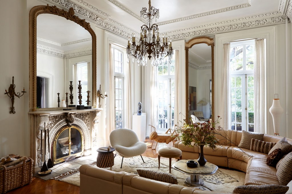 A classic European-style living room featuring towering ornate mirrors, an elaborate stone fireplace, intricate crown molding, and a curved leather sectional sofa, envisioned by interior designers
