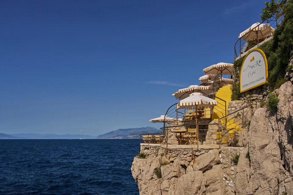 old money style, Seaside hilltop bar with outdoor tables and umbrellas overlooking the ocean.