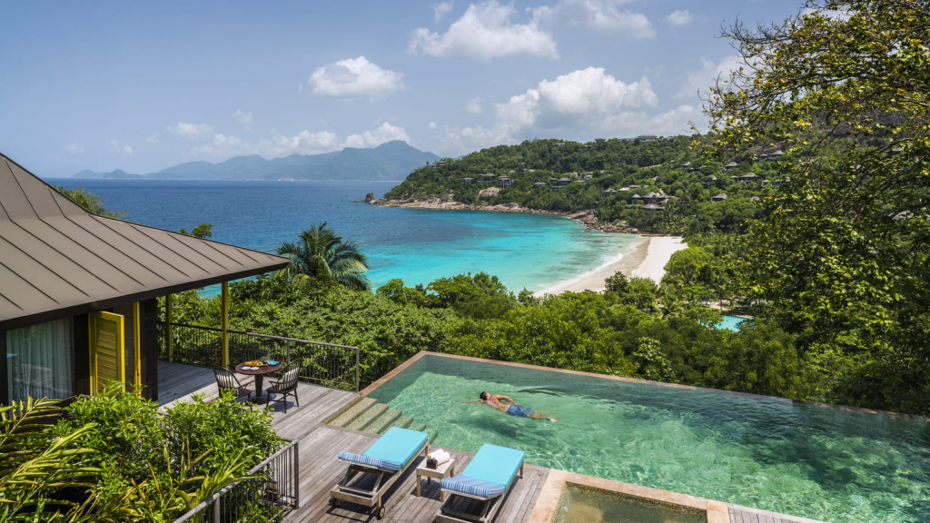 Four Seasons Hotels Resort Seychelles exterior view featuring a luxury infinity pool overlooking the tropical beach, turquoise ocean, and stunning island landscape in Seychelles.