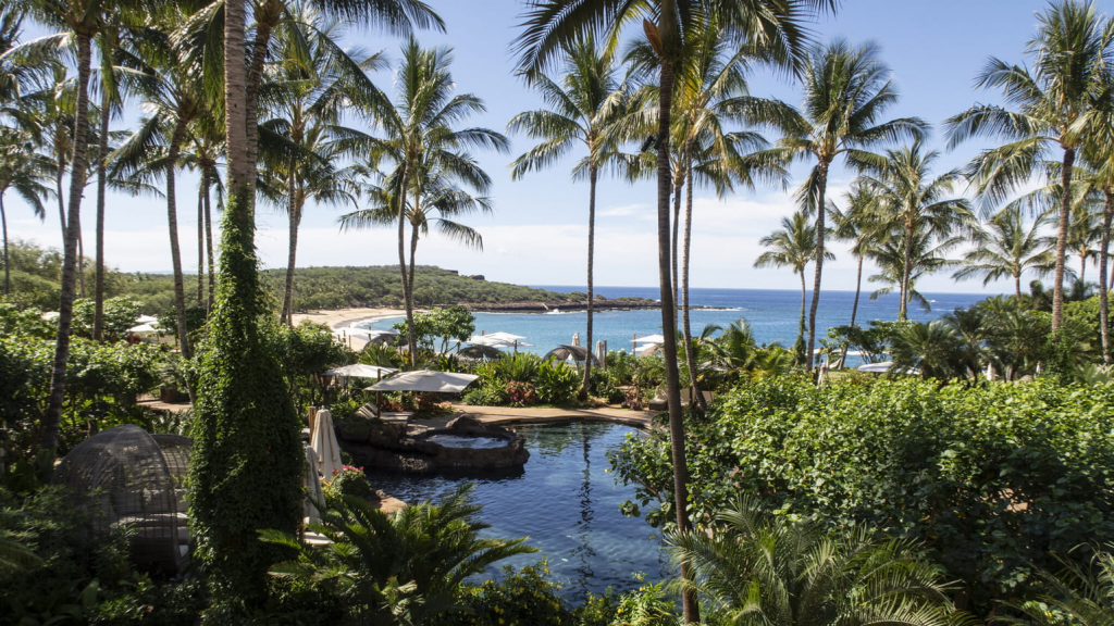 Four Seasons Hotels Resort Lanai exterior view featuring the luxury infinity pool overlooking the ocean, tropical surroundings, and island scenery in Lanai, Hawaii.