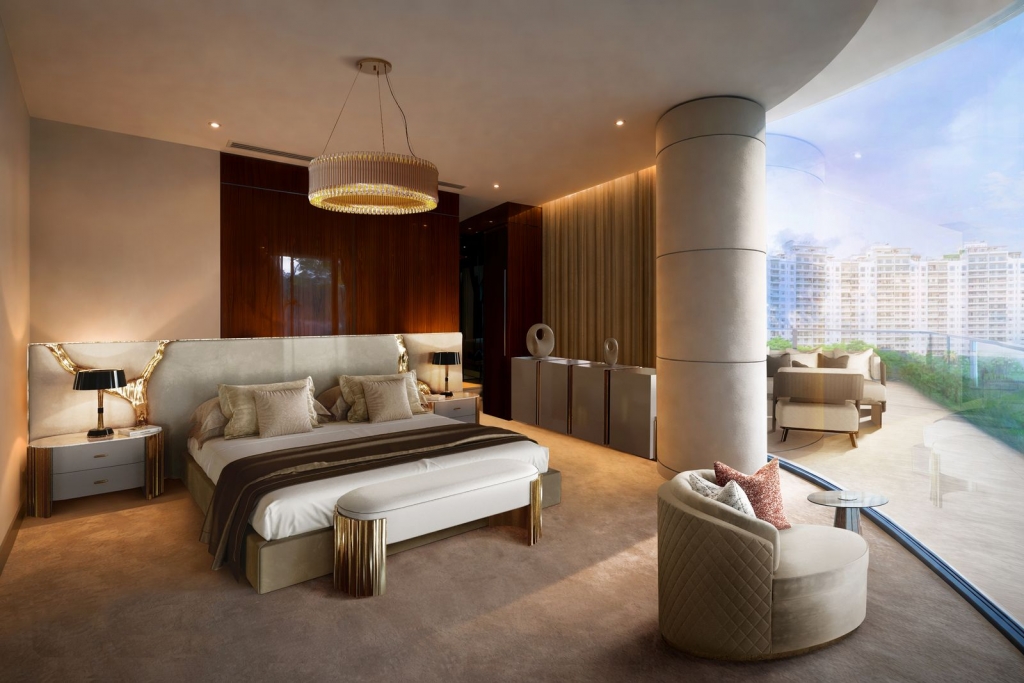 Elegant luxury bedroom with a large bed featuring an expansive beige upholstered headboard accented by organic gold metallic details. The room includes a round golden chandelier, a white cushioned bench with polished gold legs at the foot of the bed, and a curved armchair near a massive floor-to-ceiling window. The window opens up to a spacious balcony overlooking city high-rises under a clear blue sky. luxury bedrooms