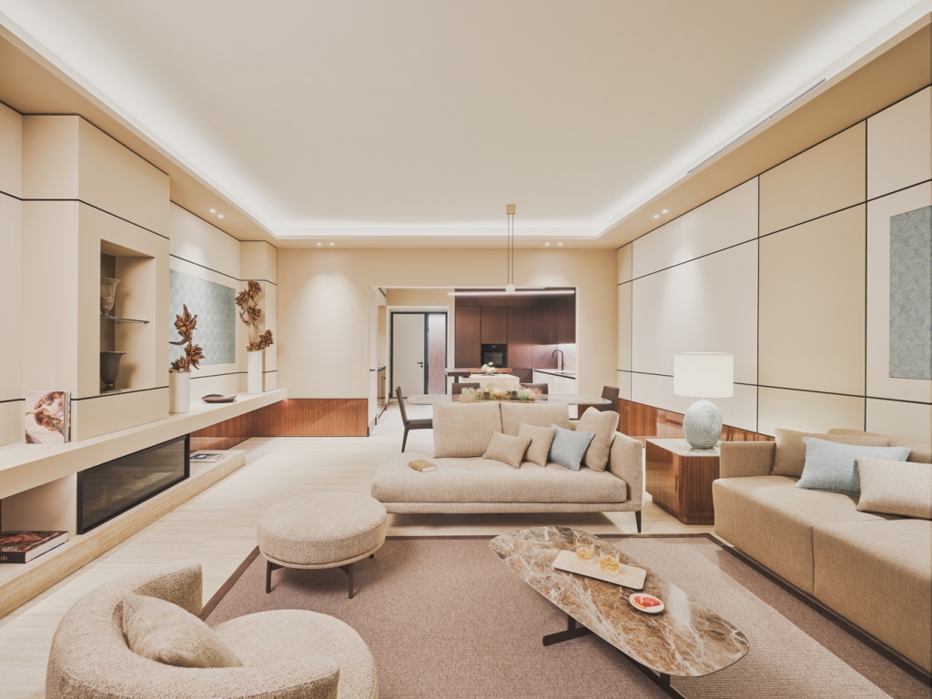 Warm neutral-toned villa living room with paneled walls, a beige sectional sofa, marble coffee table, and an open sightline to a dining area and kitchen beyond. interior designers