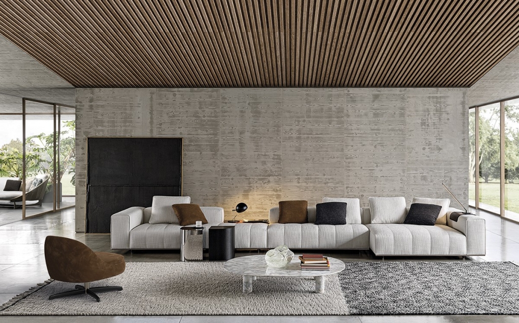 Contemporary living room with a slatted wood ceiling, board-formed concrete accent wall, channel-tufted grey sectional sofa, and a round white marble coffee table. INTERIOR DESIGNERS