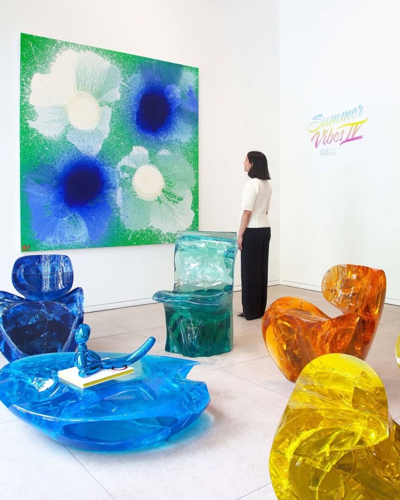 An art exhibition space showcasing vibrant translucent resin chairs in various colors and a large green and blue floral painting at PAD Saint-Tropez 2026.