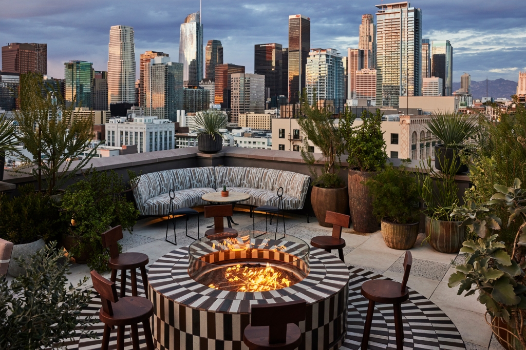 A rooftop terrace with a tiled fire pit and seating, offering panoramic views of the Los Angeles skyline at LA Proper Hotel.