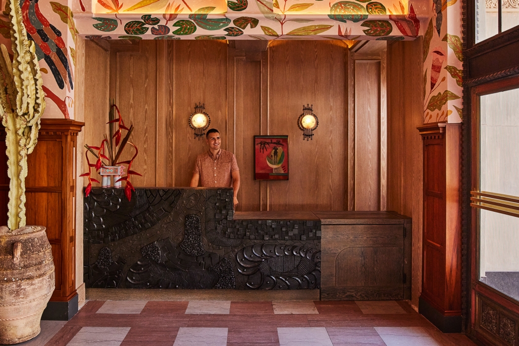 A reception desk featuring intricate dark carved panels and warm wood walls inside the lobby at LA Proper Hotel.