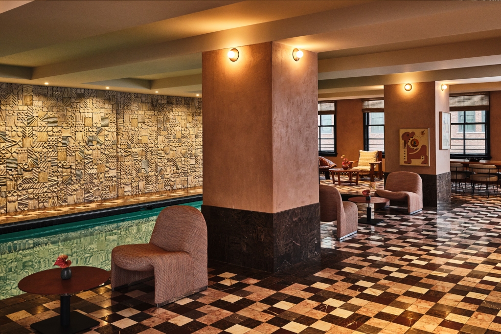 An indoor lap pool surrounded by checkered tile flooring, plush seating, and textured accent walls at LA Proper Hotel.