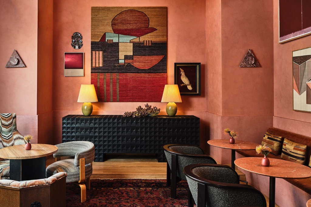 A stylish lounge area with terracotta-tinted walls, abstract artwork, and low armchairs at LA Proper Hotel.